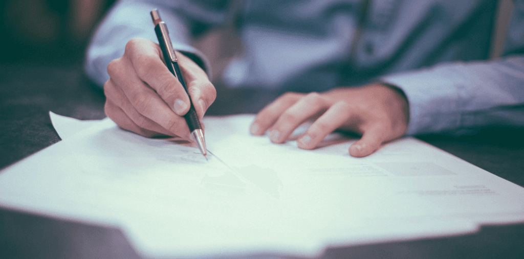 photo by Hellosequence of someone writing with pen on paper, wearing a blue business shirt. 